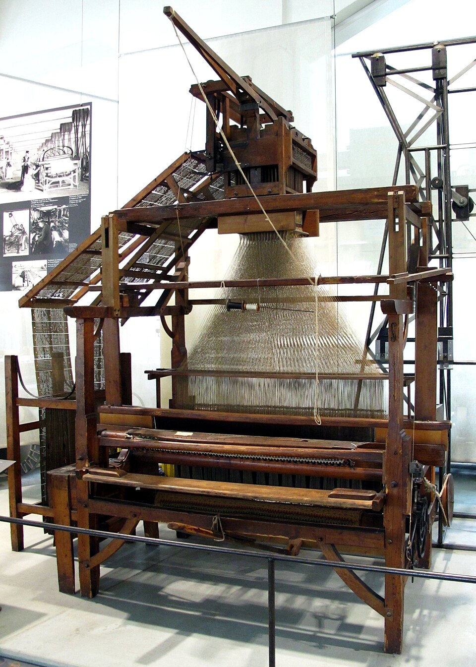 A wooden Jacquard loom in a museum, with a long chain of punched cards feeding the mechanism at its top.