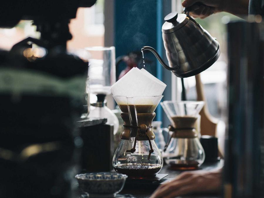 Hot water poured from a gooseneck kettle into a glass pour-over coffee maker.